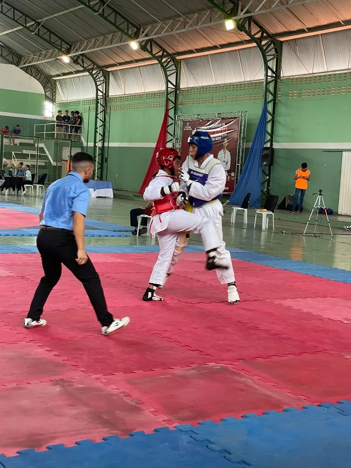 Dois praticantes de taekwondo em uma luta e o árbitro intermediando